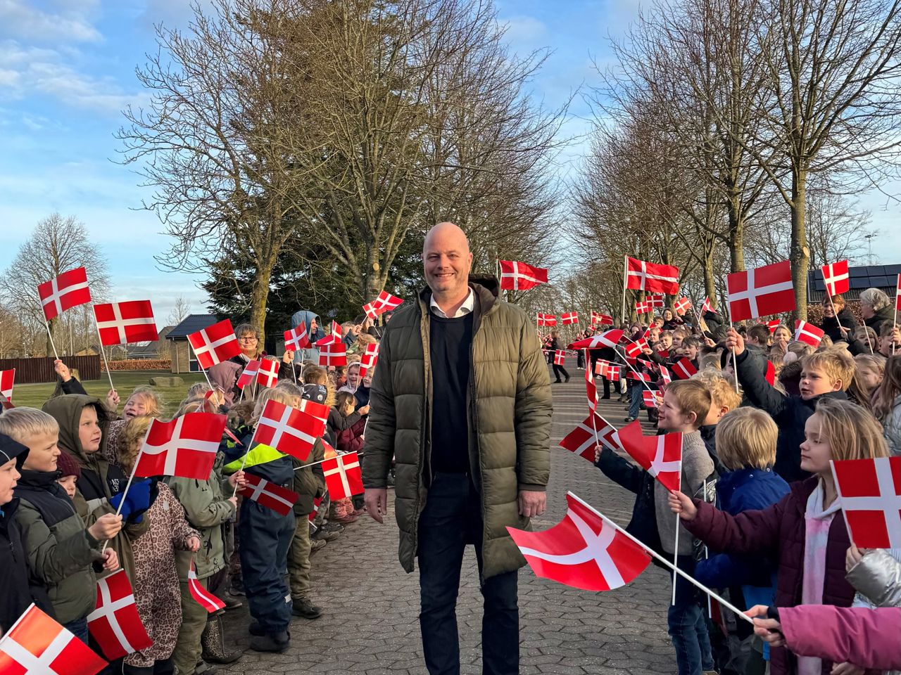 mand står i midten mellem børn der danner en flagalle