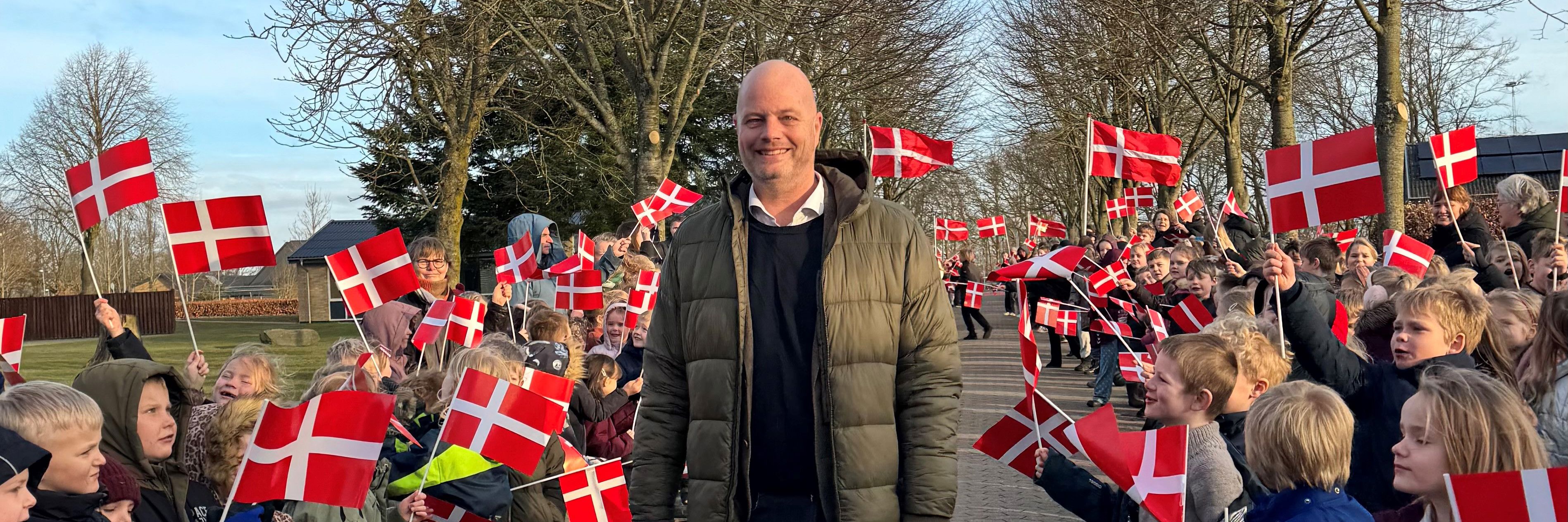 mand står i midten mellem børn der danner en flagalle
