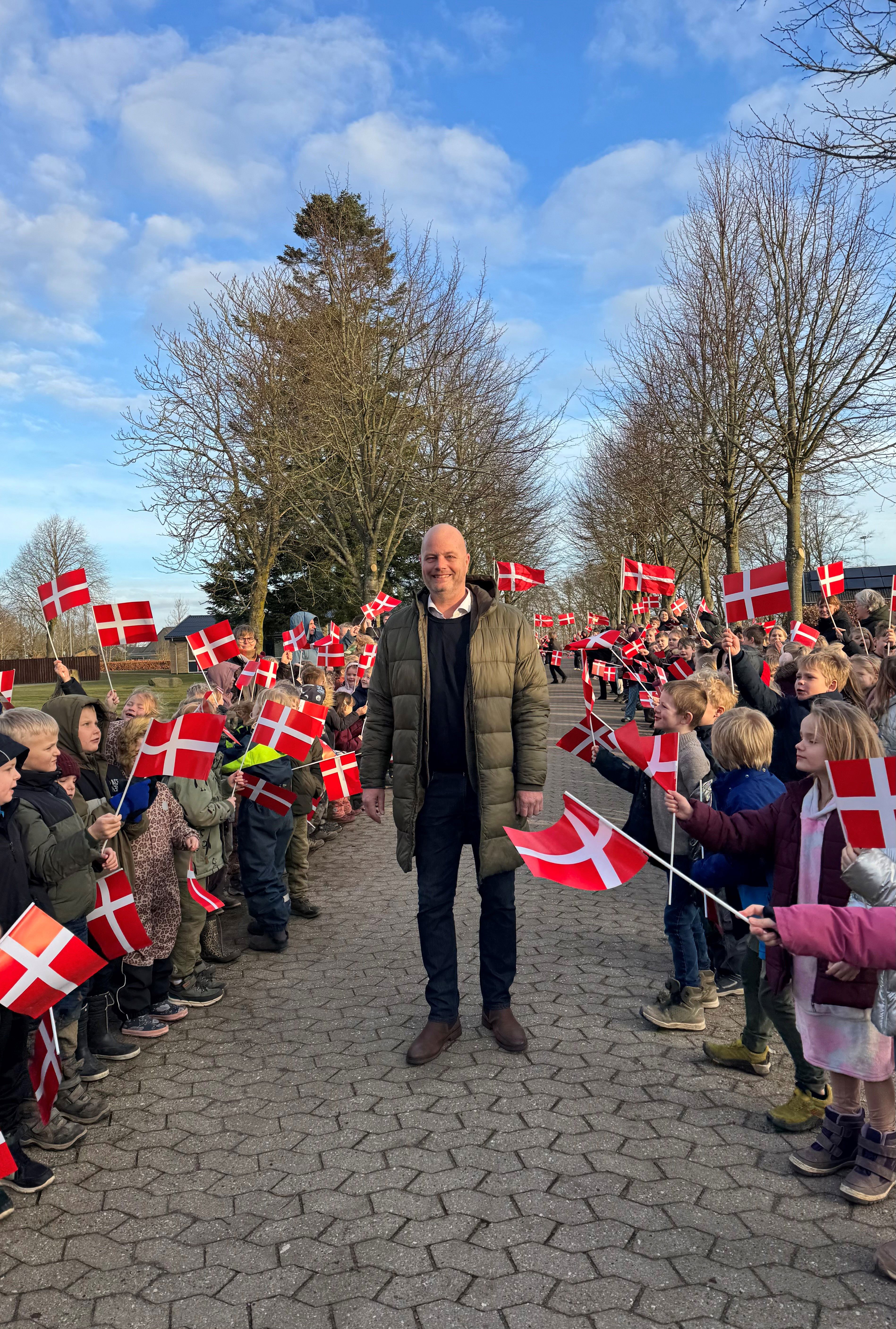 mand står i midten mellem børn der danner en flagalle